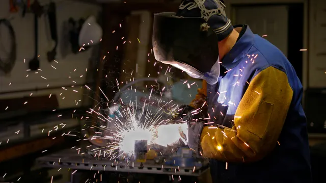 Saldatore al banco di lavoro con maschera e guanti