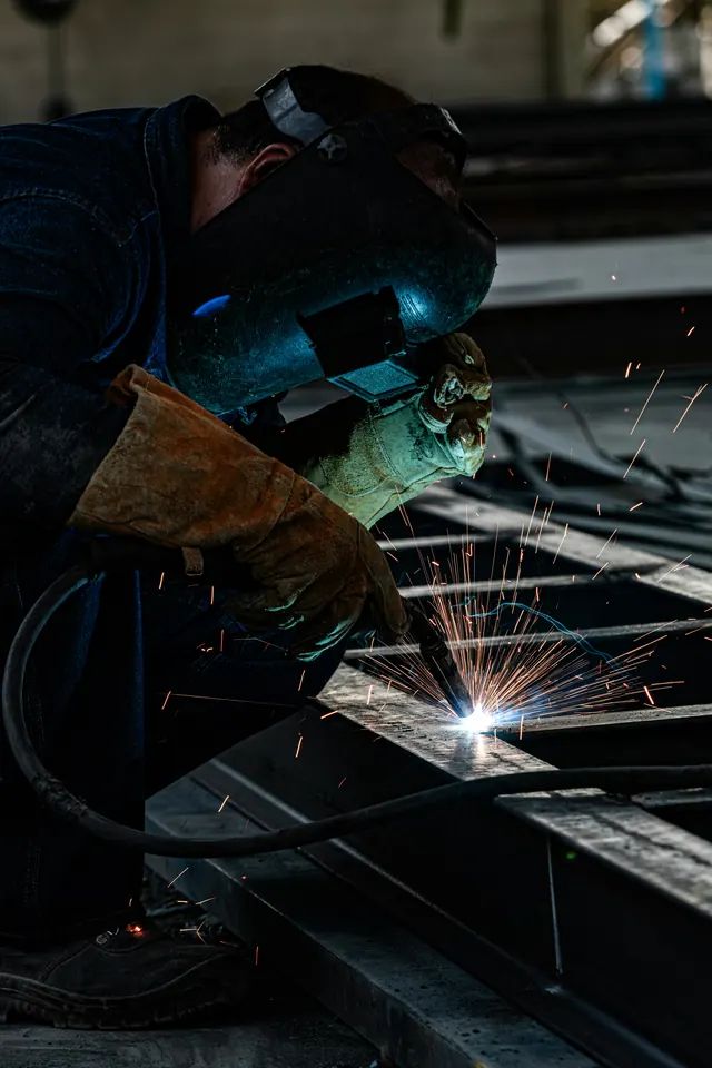 Saldatore con maschera al lavoro su una trave in acciaio